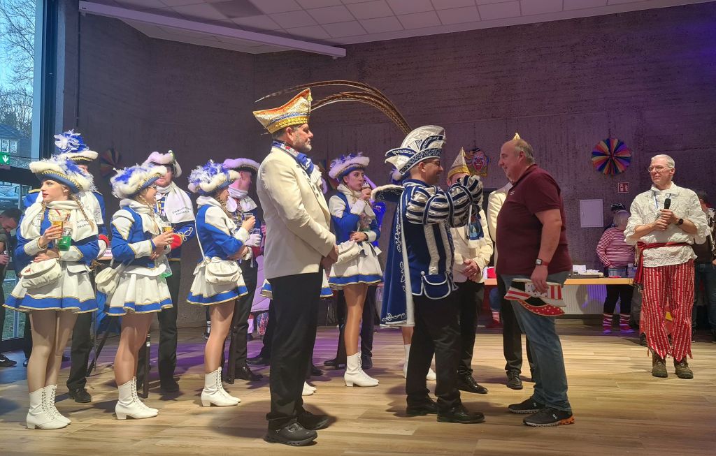 Prinz Patrick I. und die Garde stehen auf der Bühne und Blicken in den Saal. Mit zusehen ist ein Mitglied des Trägerereins. Dieses Mitglied erhält gerade vom Prinz einen Orden.